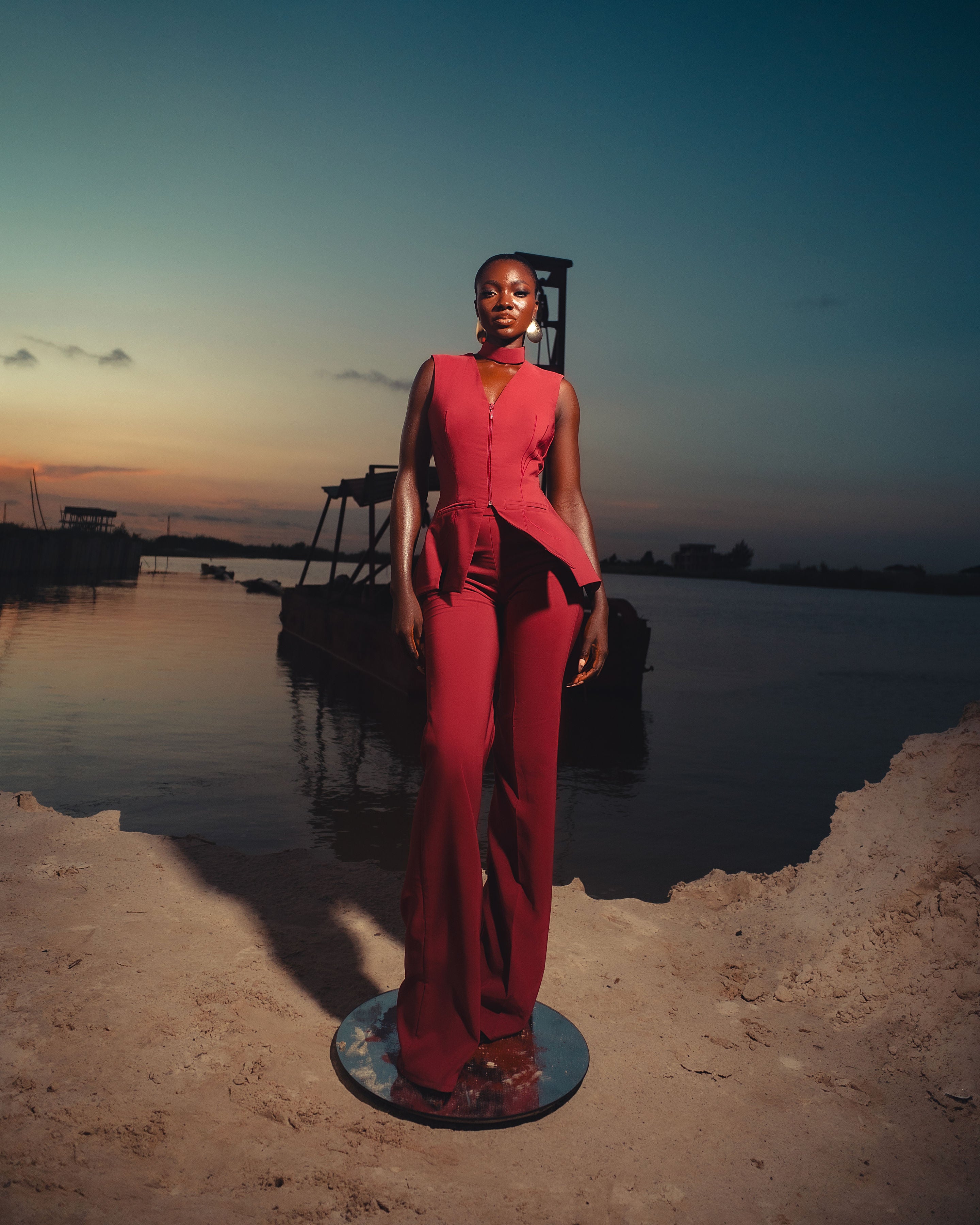 Woman in a red outfit standing by a body of water at sunset.